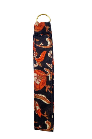 A fabric tag made from black cotton and a red, orange, and beige flower pattern, featuring a gold metal key ring at the top, shown against a plain white background.