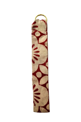 A fabric wristlet or keychain pouch with a red and beige floral pattern, featuring a gold metal ring at the top, shown against a plain light gray background.