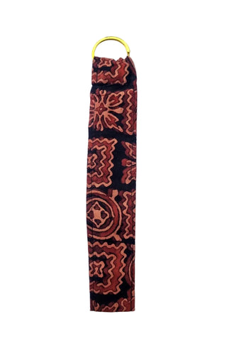 A fabric wristlet or strap featuring a red and orange geometric pattern on a black background, finished with a yellow metal ring at the top, shown against a plain white background.