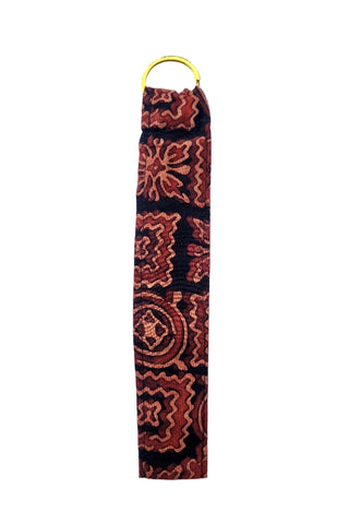 A fabric wrist strap or lanyard featuring a red and orange geometric pattern on a black background, finished with a yellow metal ring at the top, shown against a plain white background.